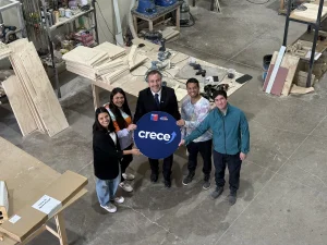 Gerente general de Sercotec y trabajadores de la empresa Crella exhiben un círculo morado con el nombre del programa Crece. De fondo se ve la planta de producción de la empresa Crella.
