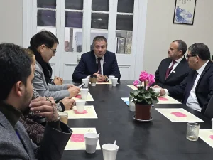El gerente general de Sercotec encabeza una reunión de trabajo junto a representantes del barrio Patronato y ejecutivos de Sercotec sentados alrededor de una mesa larga y negra. En el centro de la mesa hay una planta con flores rosadas, vasos y folletos, mientras los asistentes escuchan con atención.