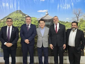 El gerente general de Sercotec y el director regional de Sercotec junto a representantes del Barrio Patronato posan juntos en fila frente a un gran fondo fotográfico. El fondo muestra un paisaje tradicional coreano con una pagoda junto a un lago, rodeada de colinas verdes bajo un cielo azul con nubes tenues.