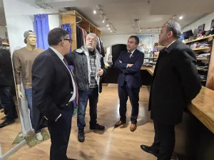 El gerente general de Sercotec, junto al director regional de Sercotec y el presidente de la Cámara de Comercio de Patronato conversan dentro de una tienda de ropa con un comerciante que lleva una bufanda tradicional palestina. Al fondo se observan percheros con prendas, repisas con ropa doblada y un maniquí.