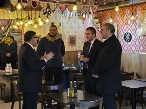 El gerente general de Sercotec, junto al director regional de Sercotec y el presidente de la Cámara de Comercio de Patronato dialogan dentro de un restaurante decorado con tapices ornamentales en las paredes e iluminación cálida. Conversan con un el administrador del local, que lleva una bufanda amarilla, en un espacio con mesas y sillas de madera.