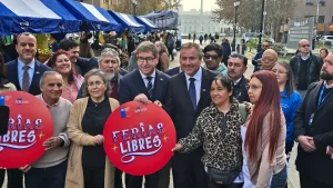 Fotografía grupal al aire libre donde un numeroso grupo de personas posa sonriente para la cámara. En el centro, el gerente general de Sercotec y el ministro de Economía sostienen un gran letrero circular rojo de Sercotec que dice "FERIAS LIBRES". A la izquierda, otra parte del grupo sostiene un cartel idéntico. Entre los presentes hay feriantes y colaboradores de distintas edades. El fondo muestra los toldos azules de los puestos de la feria libre y un entorno urbano despejado.