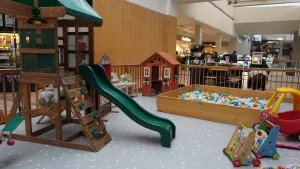 Vista de las instalaciones de Jovi Park, una plaza de juegos infantiles inserta al interior de un centro comercial, equipada con un resbaladero verde, piscina de pelotas, casita de madera y andadores.