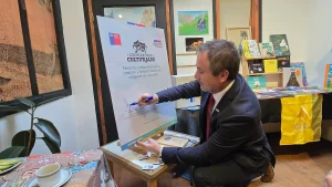 El gerente general de Sercotec firma un gran cartel que dice "Firma de compromiso por la creación y fortalecimiento de cooperativas culturales" sobre un caballete de madera.