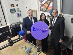 El gerente general de Sercotec, la fundadora de la empresa Cachivarte y el director regional metropolitano de Sercotec posan sonriendo mientras sostienen un cartel morado de "Capital Pioneras".