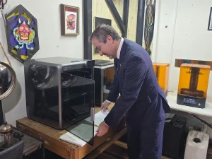 El gerente general de Sercotec se inclina para mirar dentro de una impresora 3D industrial con la puerta abierta.