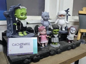Una fila de figuritas de personajes de terror y fantasía impresas en 3D y pintadas a mano están en exhibición, junto a una tarjeta de presentación de "CACHIVARTE 3D".