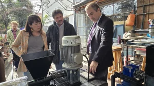Un primer plano de la jefa de Sostenibilidad FEN UChile, el fundador de Reciklast y el gerente general de Sercotec examinando una gran máquina de reciclaje con un embudo negro y un motor en un área exterior sombreada.
