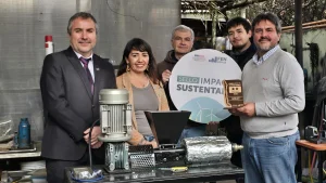 Una foto grupal de cinco personas en el taller exterior. En primera fila están el gerente general de Sercotec, la jefa de Sostenibilidad FEN UChile y el fundador de Reciklast (con el premio de madera), posando detrás de la máquina de reciclaje. Dos hombres adicionales se paran detrás, uno sosteniendo el cartel del sello.