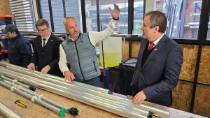 El fundador de Garage de Proyectos explica un proceso alzando la mano frente al ministro de Economía y al gerente general de Sercotec, quienes escuchan con atención junto a un mesón con tubos metálicos de producción.