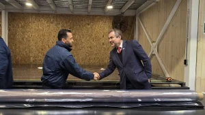 El gerente general de Sercotec sonríe mientras estrecha la mano de un trabajador con chaqueta azul en el taller, con un rollo de plástico transparente en primer plano.