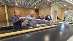 El gerente general de Sercotec, el fundador de Garage de Proyectos, el ministro de Economía y el director regional de Sercotec (de izquierda a derecha) examinan juntos un rollo de plástico transparente extendido sobre una gran mesa de trabajo en un taller.