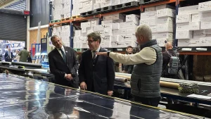 El fundador de Garage de Proyectos señala con la mano y explica un proceso de producción al ministro de Economía y al director regional de Sercotec, en un taller con estanterías llenas de cajas de fondo.