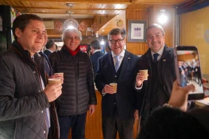 Autoridades y locatarios posan sonrientes sosteniendo vasos de café, mientras alguien les toma una foto con un celular.