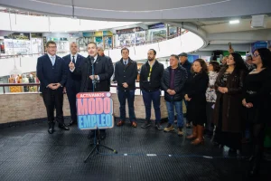 Vista general de un punto de prensa en el interior del Caracol Ñuñoa, con autoridades y locatarios escuchando al gerente general de Sercotec frente a un letrero que dice "Activamos Modo Empleo".
