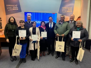 Foto grupal de autoridades de Sercotec y el Ministerio de Economía junto a representantes de cooperativas rurales beneficiarias del programa Fortalecimiento de Cooperativas. Varios sostienen documentos y bolsas de tela con el logo de Sercotec. Al fondo, un letrero de "Centros de Desarrollo de Negocios".