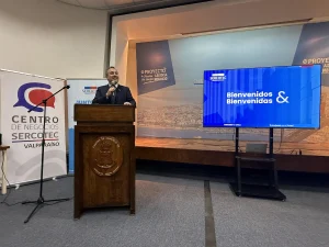 El gerente general de Sercotec, de traje, habla desde un podio de madera que tiene el escudo de la Cámara de Comercio de Valparaíso. A su izquierda hay un pendón del "Centro de Negocios Sercotec Valparaíso" y a su derecha una pantalla LED con el mensaje "Bienvenidos & Bienvenidas".