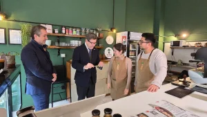 Los dos dueños de Inti Mapu, en delantales, le muestran y explican algo pequeño que sostiene el ministro de Economía. El gerente general de Sercotec observa la interacción sonriendo.