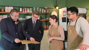 Las autoridades y los dueños de Inti Mapu están agrupados detrás del mostrador de la pastelería. El gerente general de Sercotec señala un folleto abierto sobre el mesón mientras el ministro de Economía y los dueños miran.