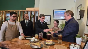 El ministro de Economía, el gerente general de Seroctec y la dueña del local Inti Mapu sostienen platos con porciones de tarta frente a una mesa de madera. Junto al director regional de Sercotec sonríen y miran una muestra de pasteles.