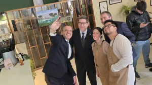 Autoridades y emprendedores se toman una selfi. El director regional de Sercotec estira el brazo con su teléfono, mientras el ministro de Economía, los dueños del local y el gerente general de Sercotec posan sonriendo hacia la cámara. De fondo se ve la decoración del local y otra persona ajena al grupo.